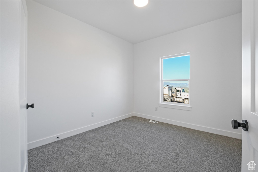 Empty room featuring baseboards, dark colored carpet, and visible vents