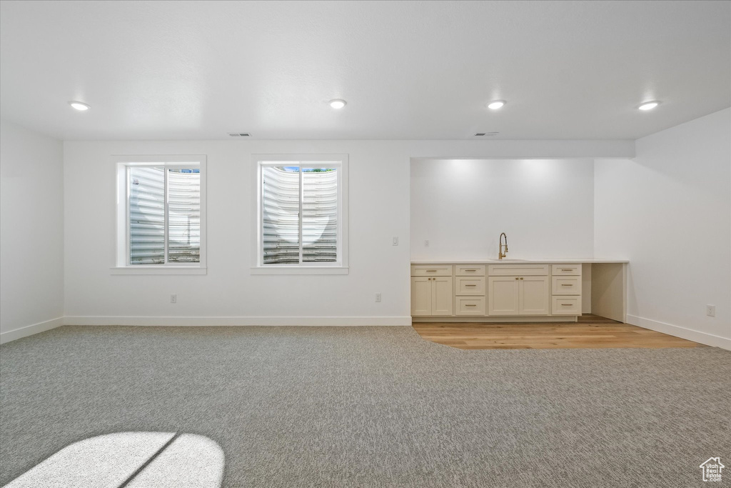Unfurnished living room with light colored carpet, recessed lighting, baseboards, and a sink