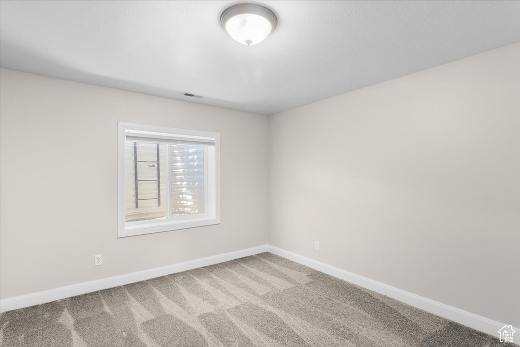 Empty room featuring carpet flooring, visible vents, and baseboards