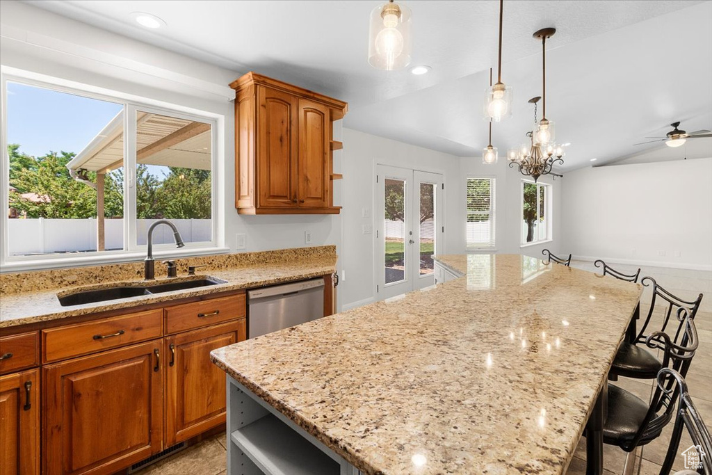 Kitchen featuring french doors, stainless steel dishwasher, a center island, light stone counters, and a sink