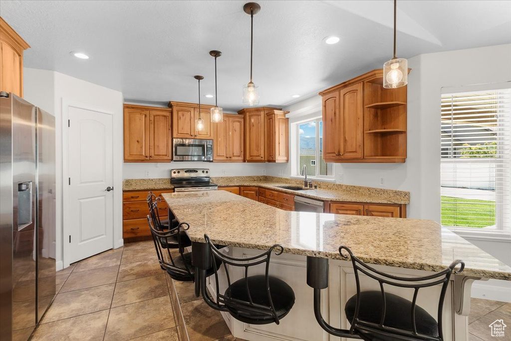 Kitchen featuring a sink, light stone counters, a kitchen bar, a kitchen island, and appliances with stainless steel finishes