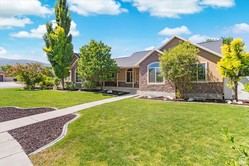 View of front of property featuring a mountain view, stucco siding, stone siding, and a front yard