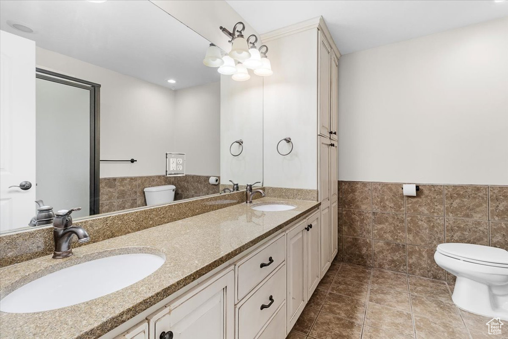 Full bathroom with toilet, tile walls, a wainscoted wall, and a sink