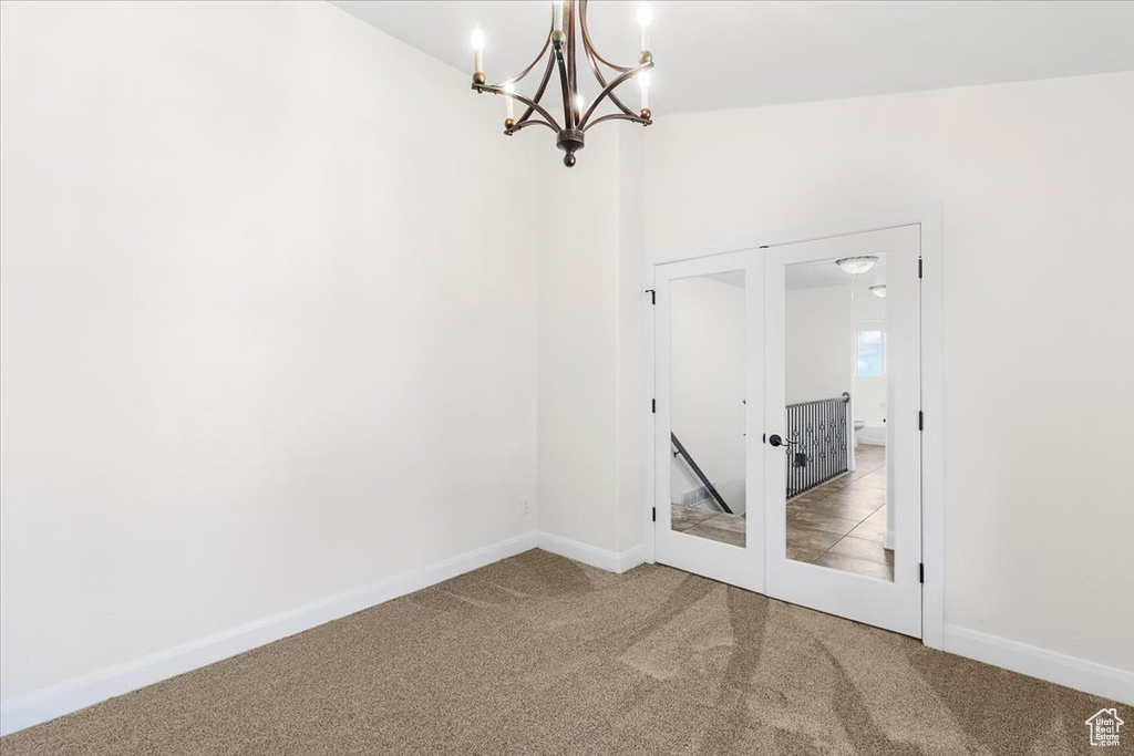 Empty room with a chandelier, carpet, baseboards, and french doors