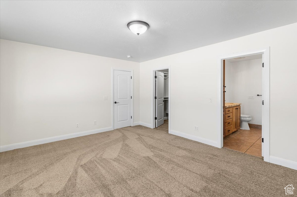 Unfurnished bedroom with light colored carpet, connected bathroom, baseboards, and a walk in closet