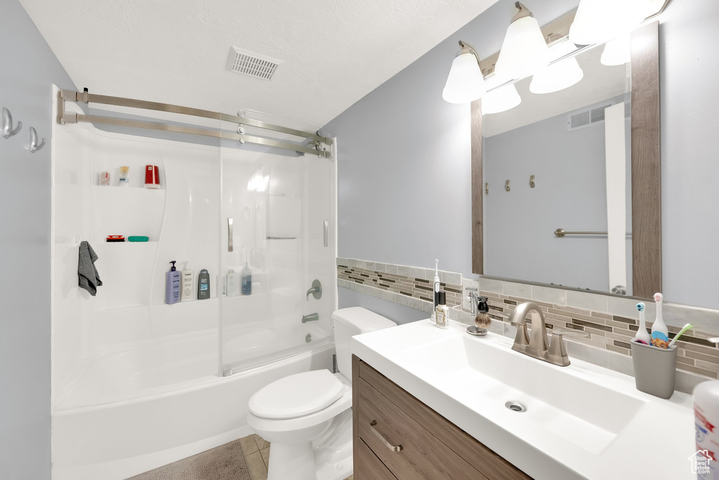 Full bath featuring toilet, enclosed tub / shower combo, visible vents, vanity, and decorative backsplash