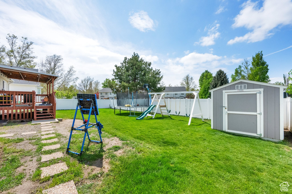 View of yard featuring a trampoline, a shed, a fenced backyard, a wooden deck, and a playground