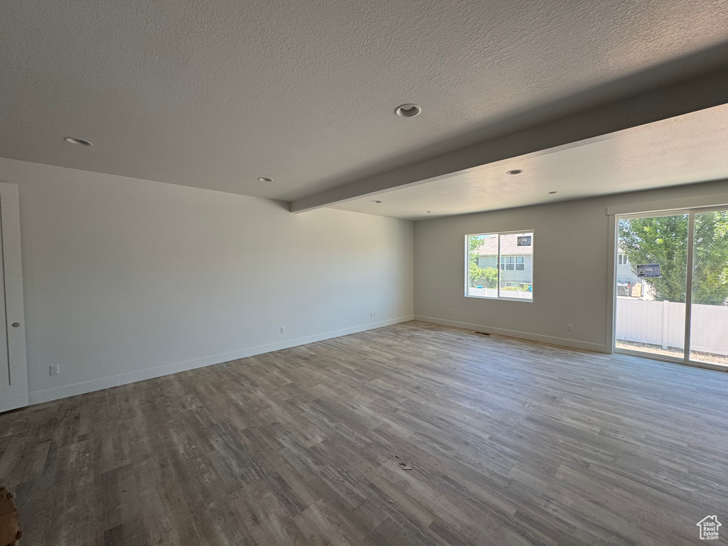 Empty room featuring wood finished floors, a textured ceiling, baseboards, beam ceiling, and recessed lighting