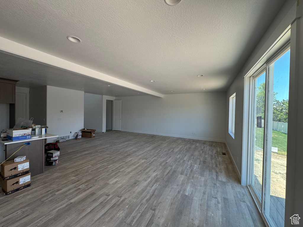 Unfurnished living room featuring wood finished floors, a textured ceiling, baseboards, and recessed lighting