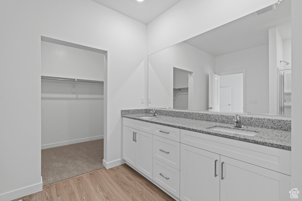 Bathroom with double vanity, wood finished floors, a spacious closet, and a sink