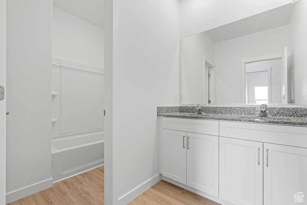 Full bath featuring double vanity, wood finished floors, baseboards, and a sink