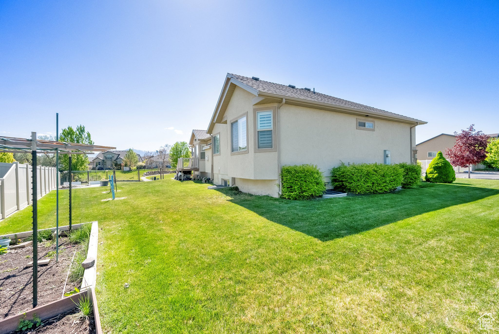 View of side of property featuring a yard, a vegetable garden, stucco siding, and fence