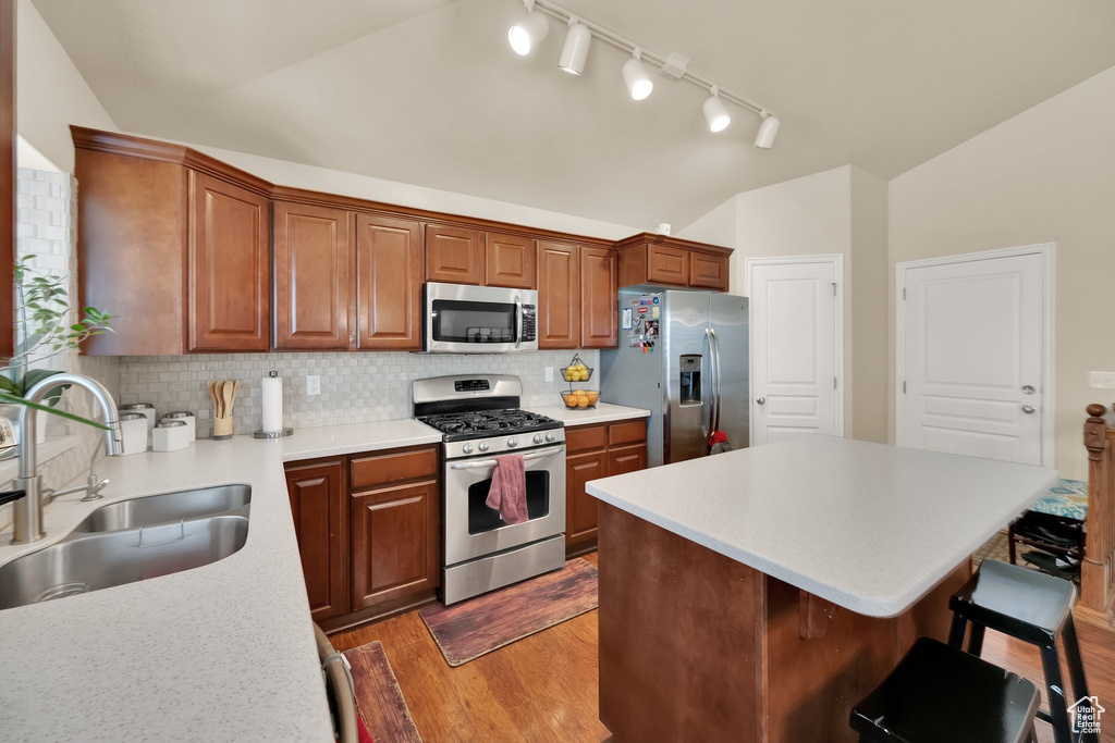 Kitchen featuring a breakfast bar area, wood finished floors, a sink, appliances with stainless steel finishes, and lofted ceiling