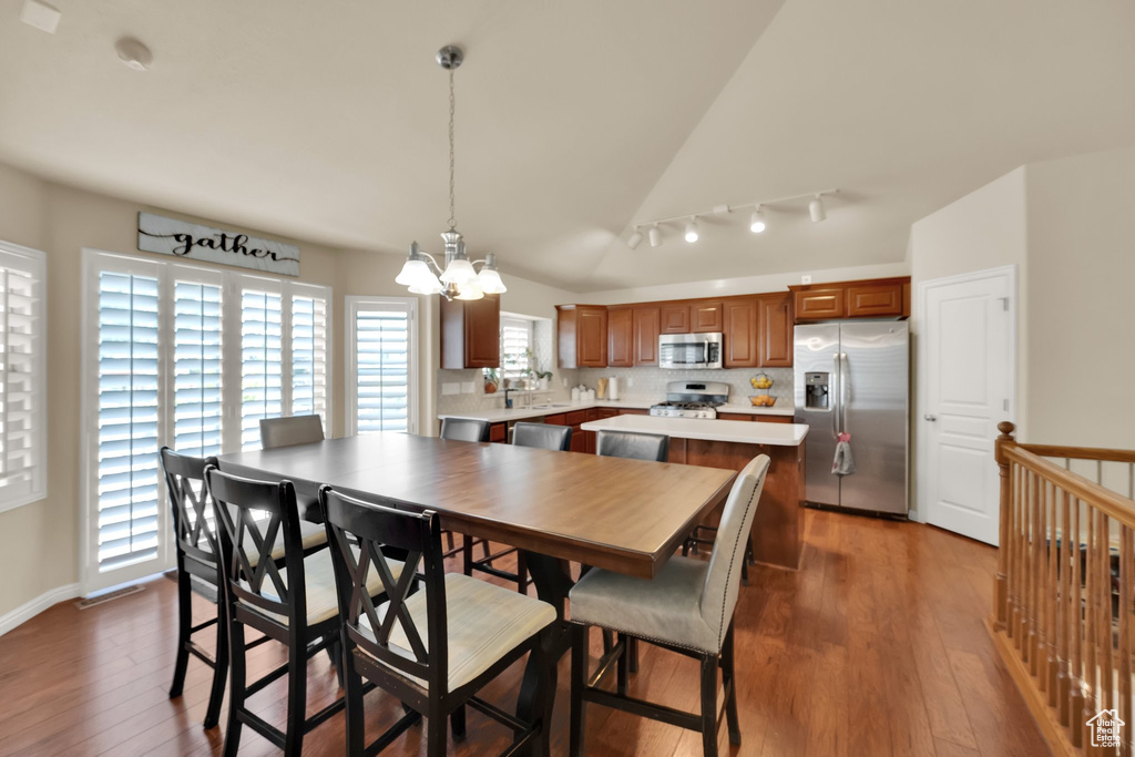 Dining area featuring vaulted ceiling, rail lighting, a chandelier, and wood finished floors