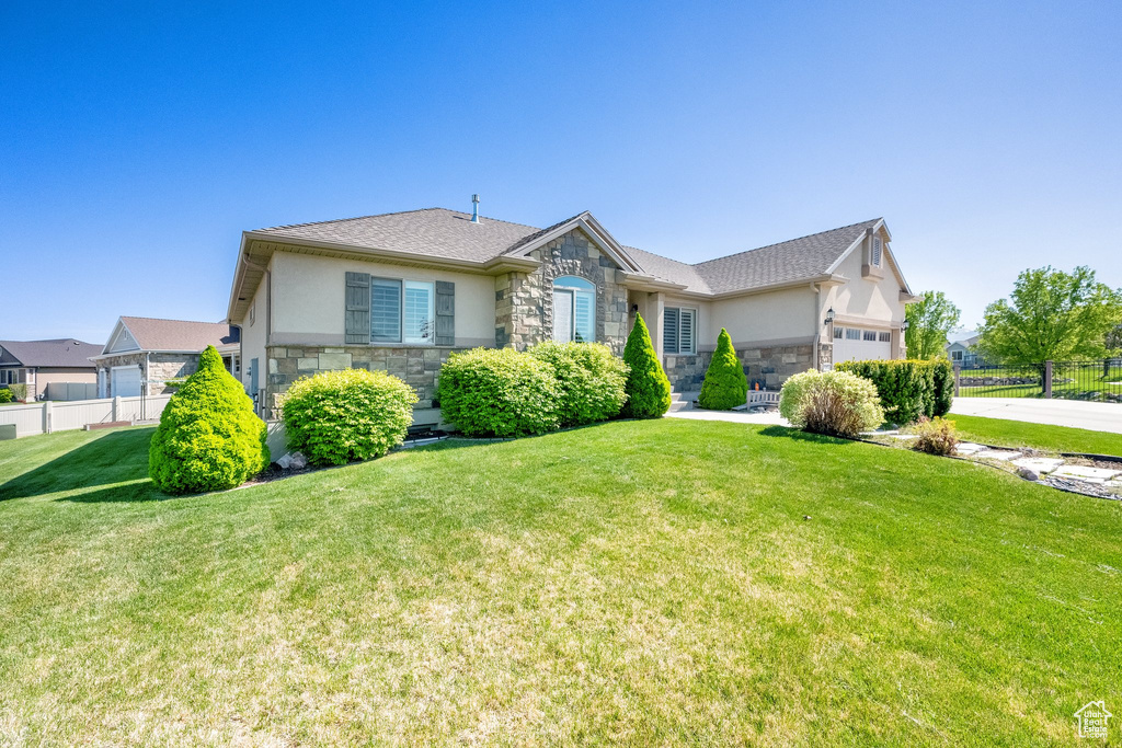 View of front of house with stone siding, a garage, stucco siding, fence, and a front lawn