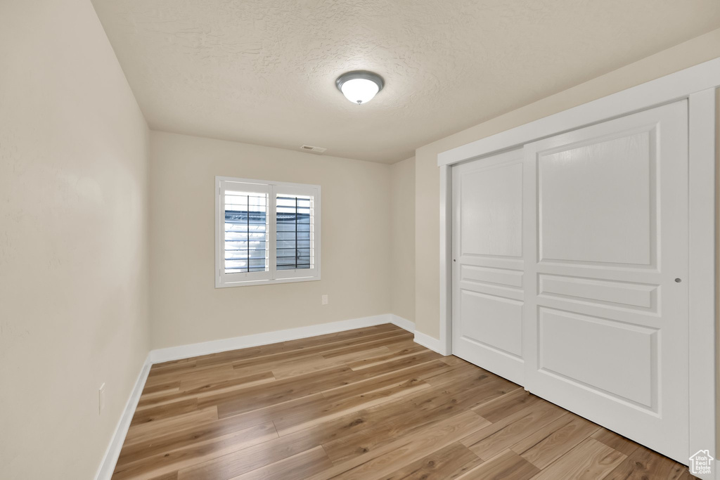 Unfurnished bedroom featuring light wood finished floors, a closet, a textured ceiling, visible vents, and baseboards