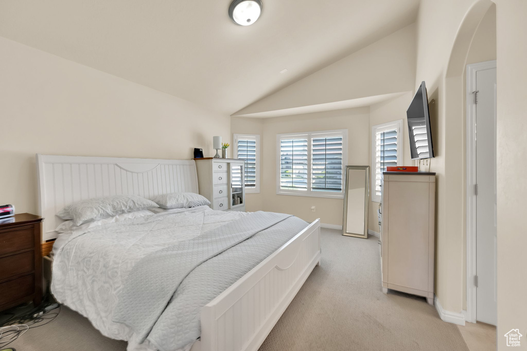 Bedroom featuring lofted ceiling, light carpet, arched walkways, and baseboards