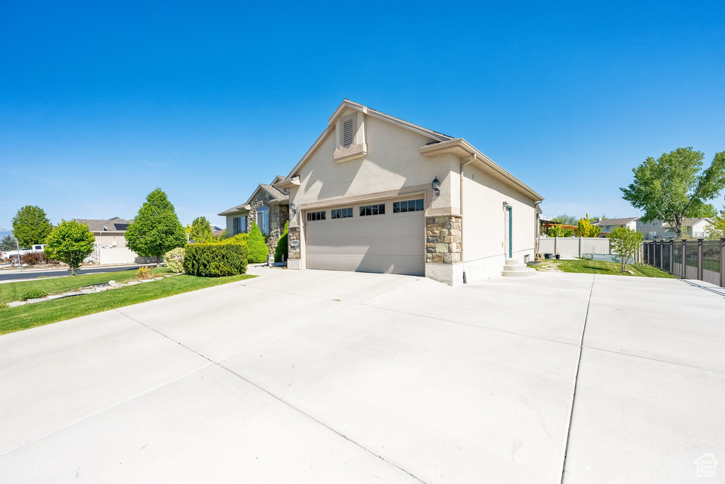 View of side of home with fence, an attached garage, stone siding, driveway, and stucco siding