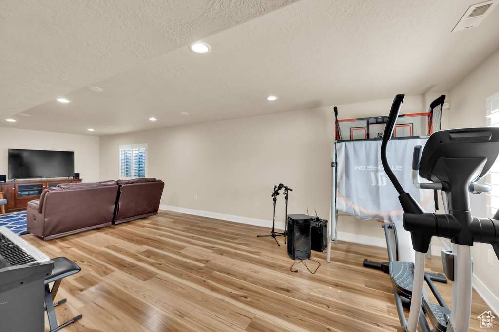Exercise room featuring baseboards, light wood-style flooring, and a textured ceiling