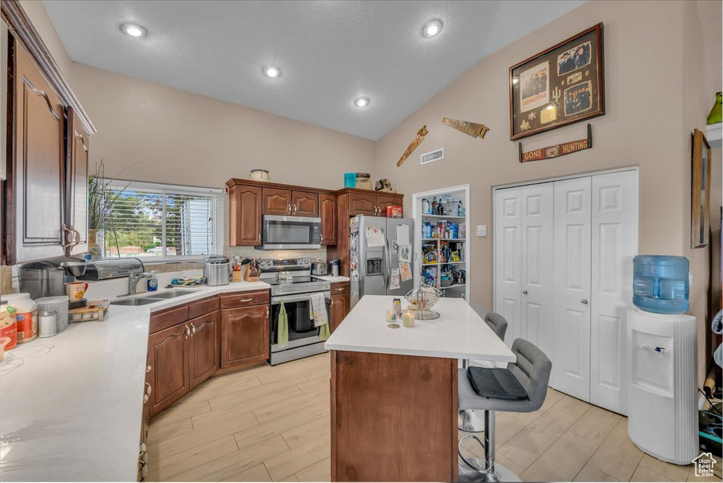 Kitchen featuring stainless steel appliances, tasteful backsplash, a breakfast bar, high vaulted ceiling, and a kitchen island