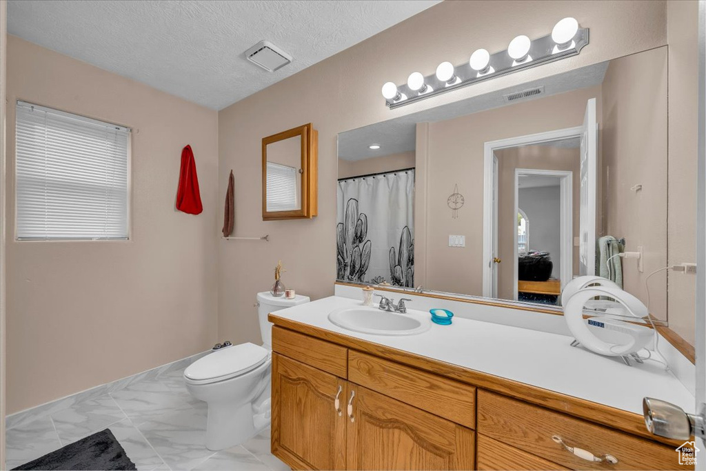 Full bath with marble finish floor, vanity, toilet, and visible vents
