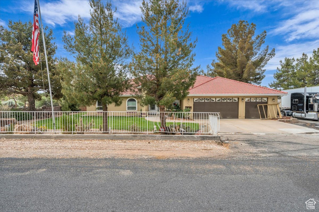 View of front facade featuring a tile roof, concrete driveway, a garage, stucco siding, and a fenced front yard