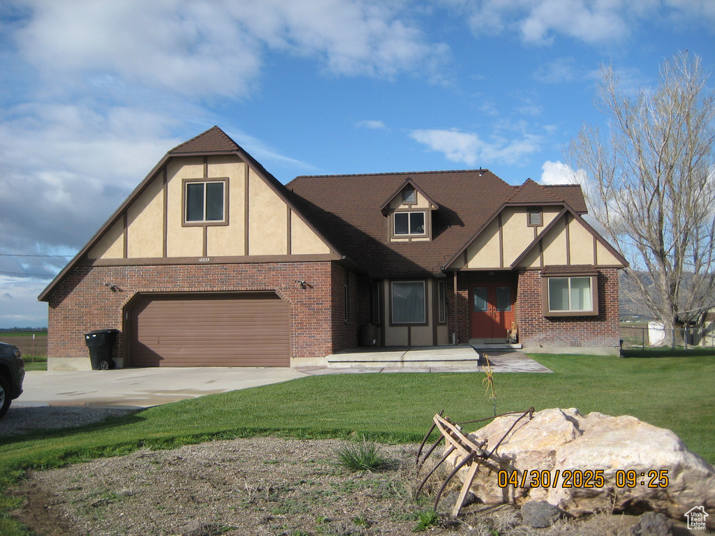 Tudor home featuring a garage, brick siding, driveway, and a front yard