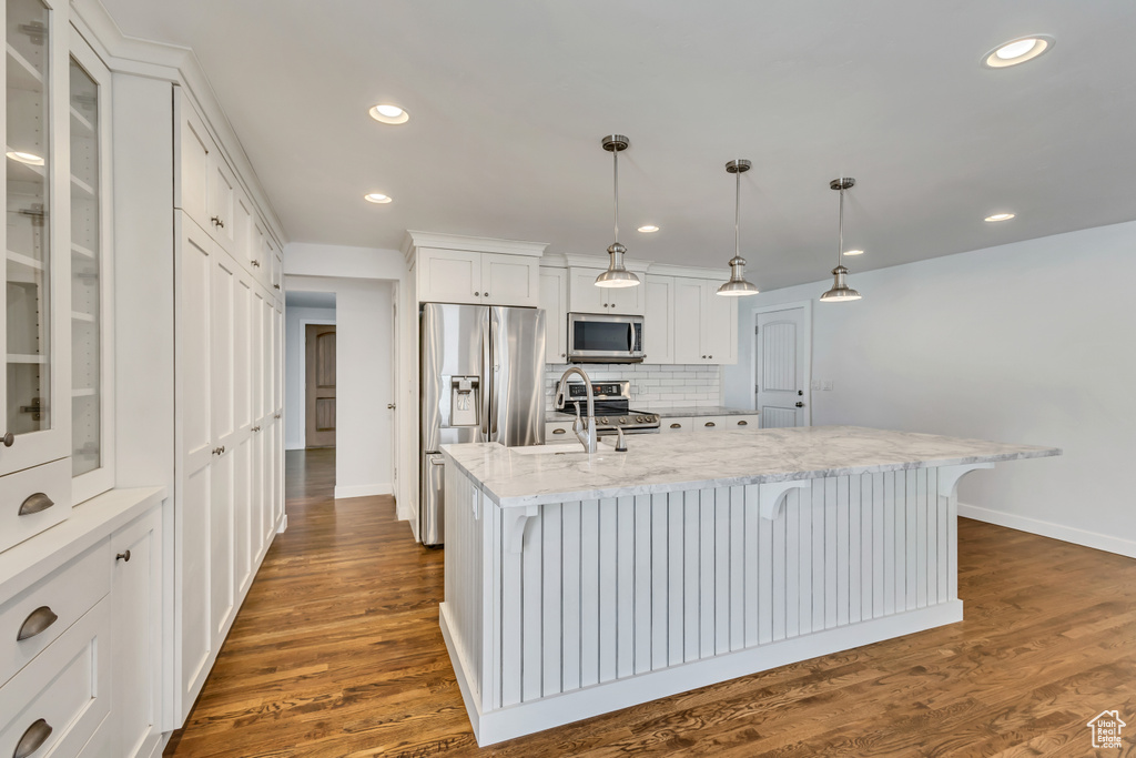 Kitchen with stainless steel appliances, tasteful backsplash, glass insert cabinets, white cabinets, and baseboards