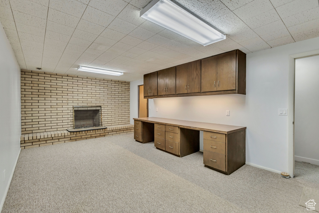 Unfurnished office featuring baseboards, a brick fireplace, light colored carpet, and built in study area