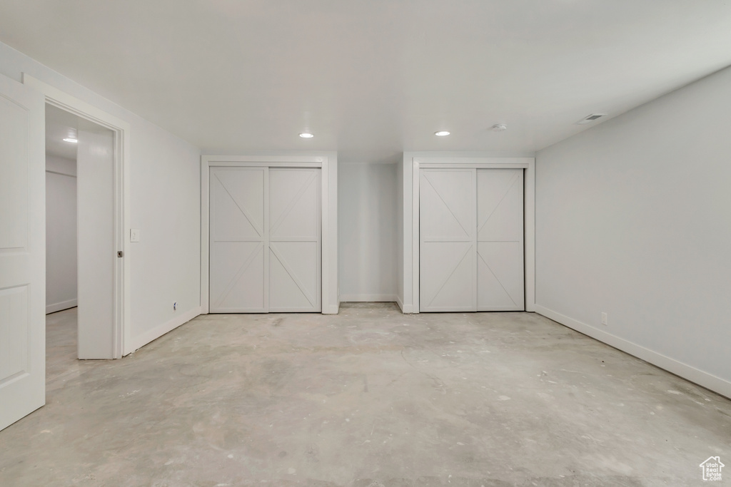 Unfurnished bedroom featuring two closets, concrete flooring, baseboards, and recessed lighting