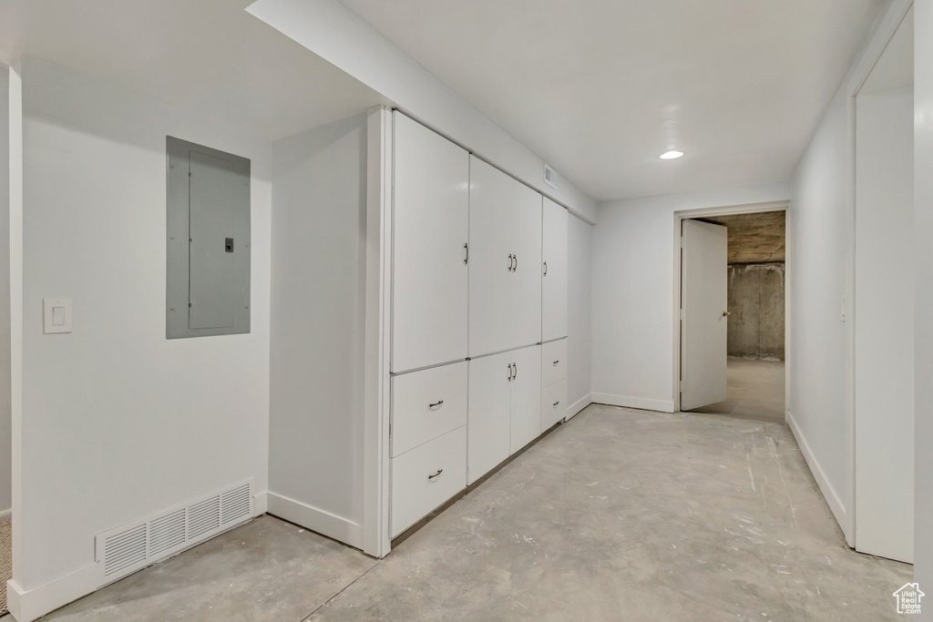 Hall featuring baseboards, unfinished concrete flooring, visible vents, and electric panel