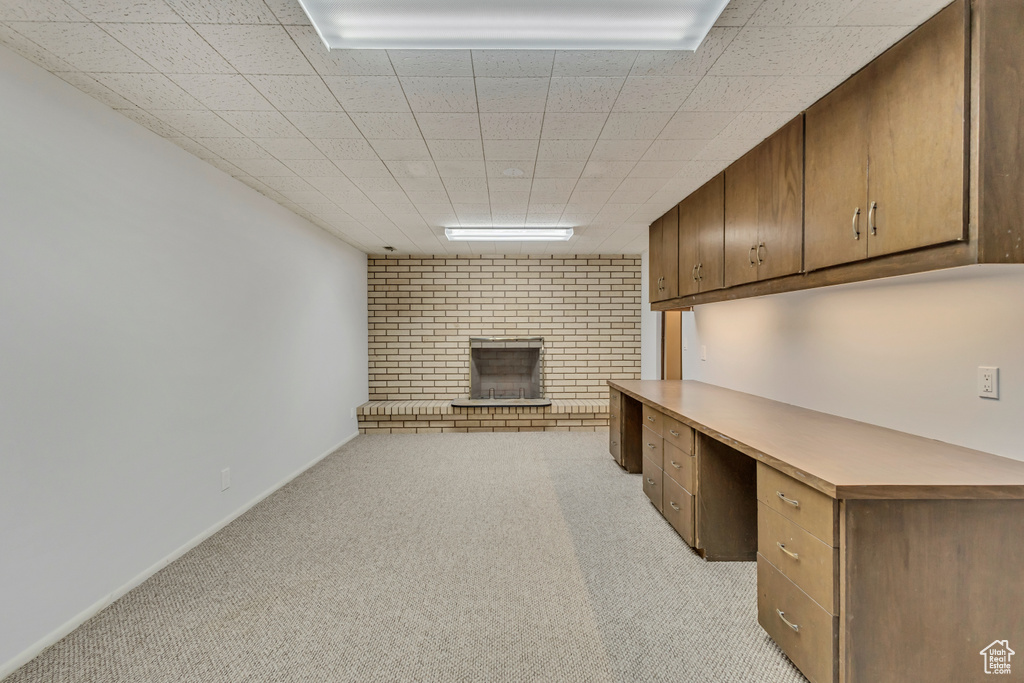 Unfurnished office featuring baseboards, light carpet, a fireplace, and built in study area