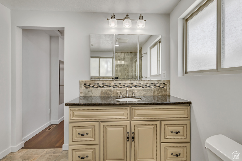 Bathroom featuring toilet, tasteful backsplash, vanity, a stall shower, and baseboards