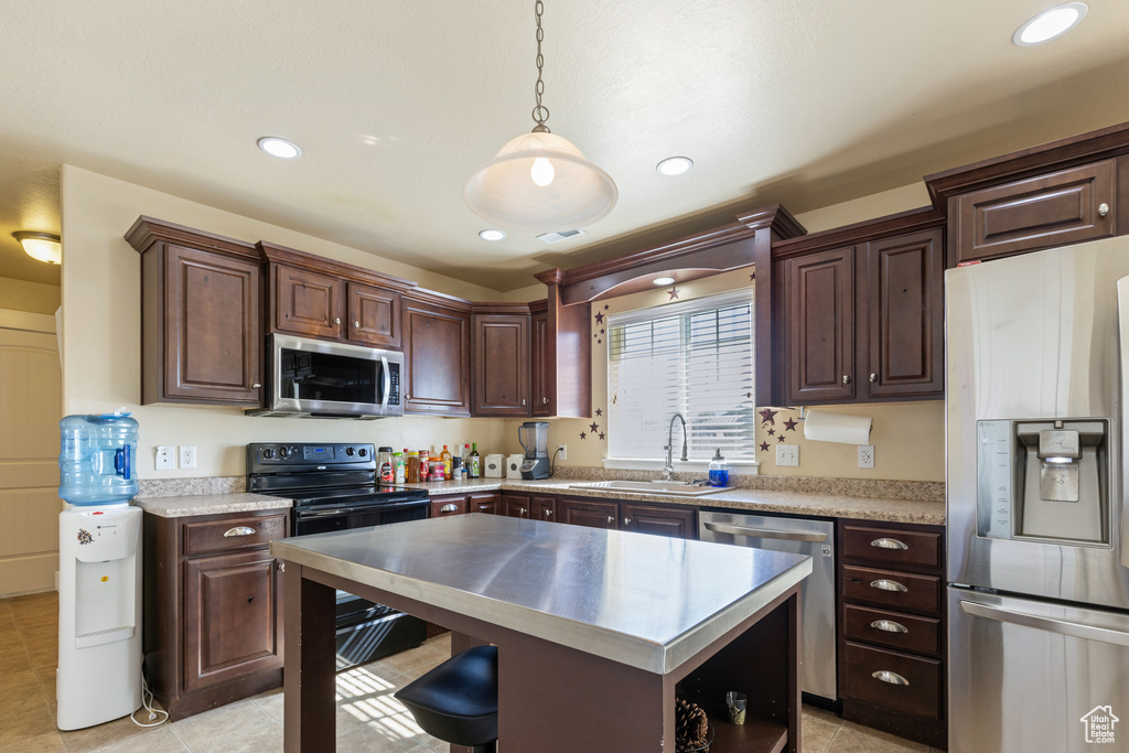Kitchen with a sink, pendant lighting, light countertops, dark brown cabinets, and appliances with stainless steel finishes
