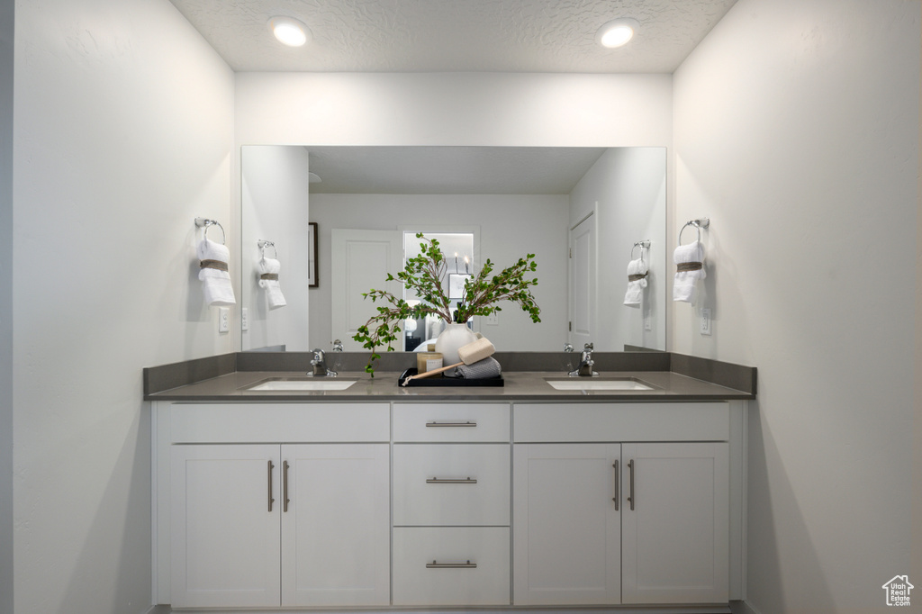 Full bath with a textured ceiling, recessed lighting, double vanity, and a sink