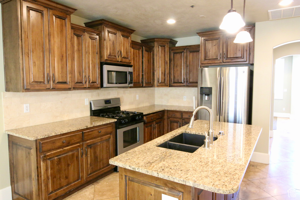 Kitchen with light stone counters, visible vents, a sink, arched walkways, and stainless steel appliances