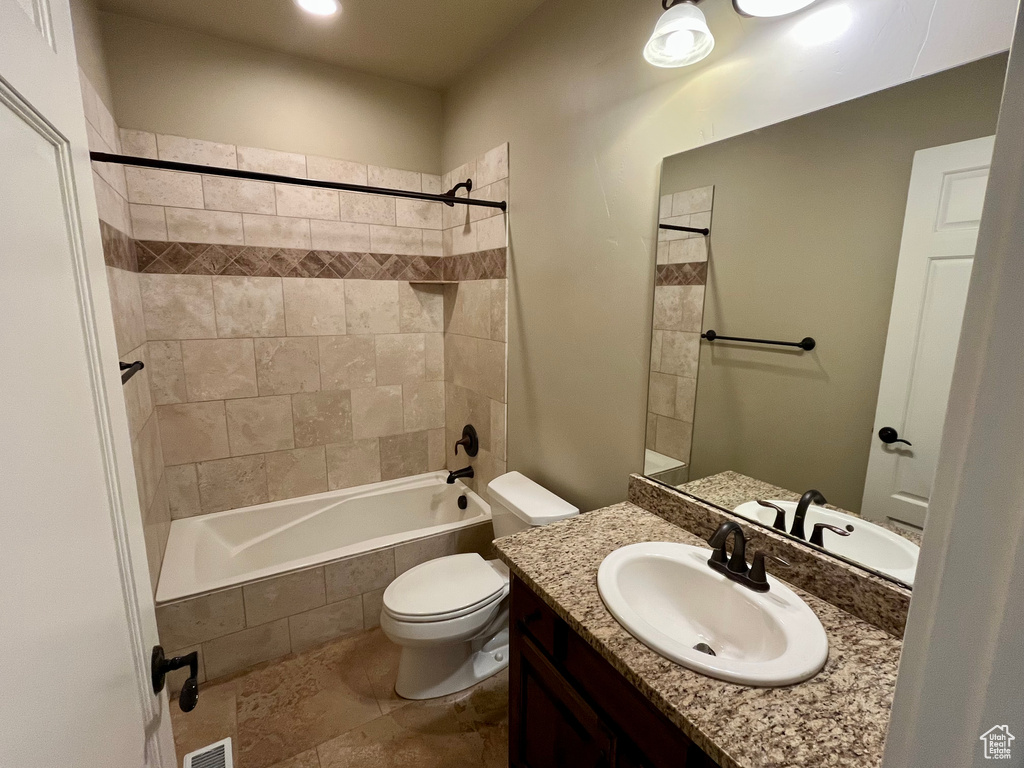 Bathroom featuring vanity, toilet, tiled shower / bath combo, and visible vents
