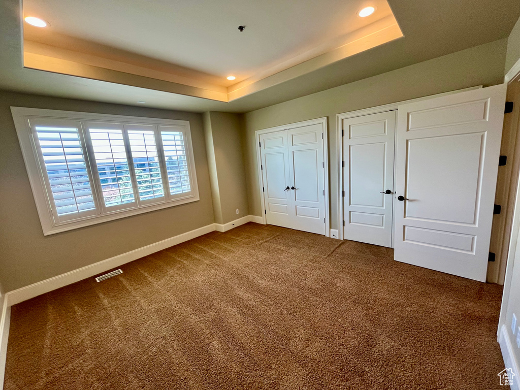 Unfurnished bedroom with a tray ceiling, dark carpet, baseboards, and multiple closets