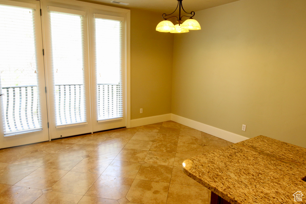 Unfurnished dining area featuring light tile patterned flooring, a notable chandelier, baseboards, and visible vents