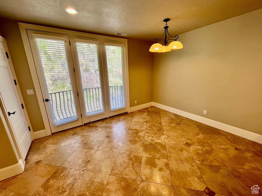 Unfurnished dining area featuring a textured ceiling, a notable chandelier, baseboards, and visible vents