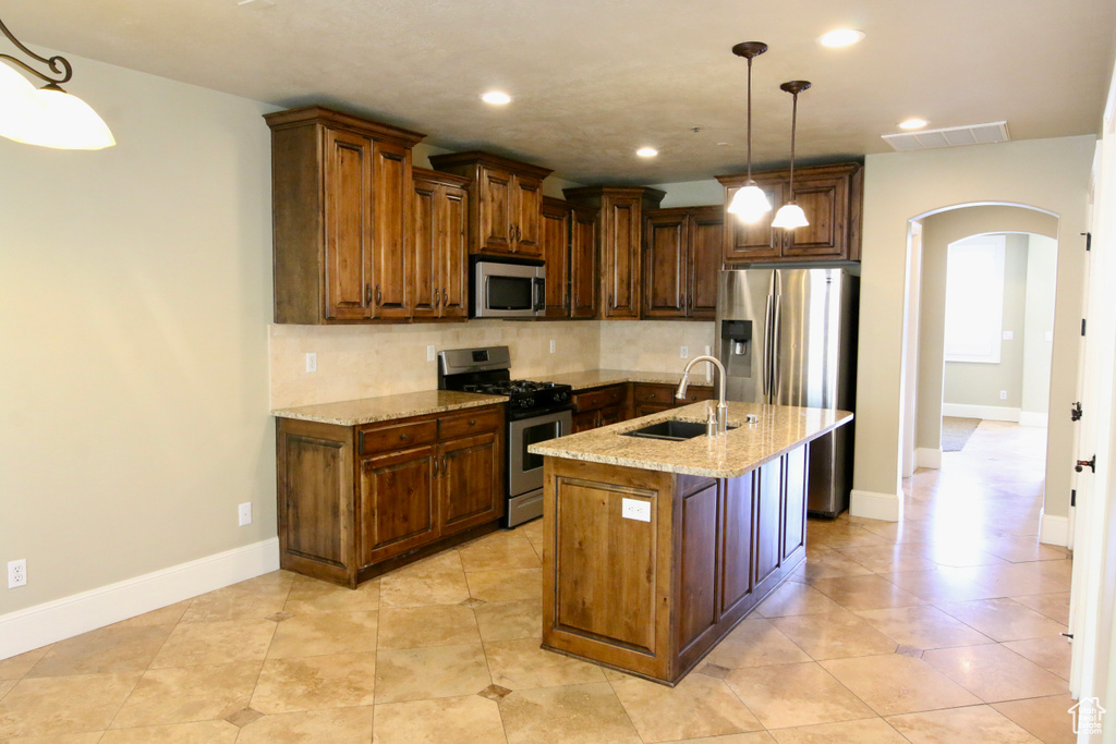 Kitchen featuring a sink, backsplash, arched walkways, light stone countertops, and appliances with stainless steel finishes