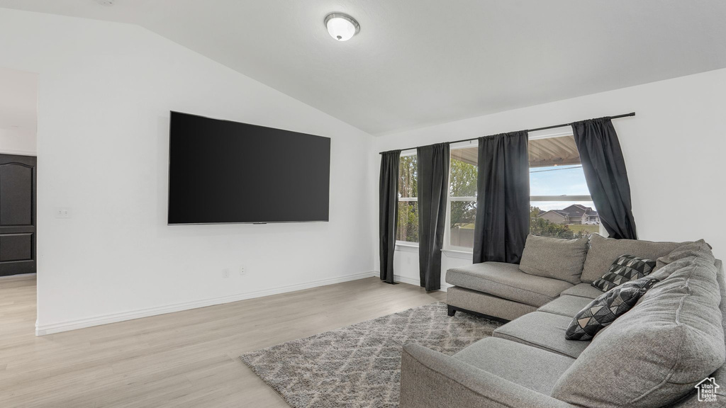 Living area with lofted ceiling, baseboards, and light wood-style flooring