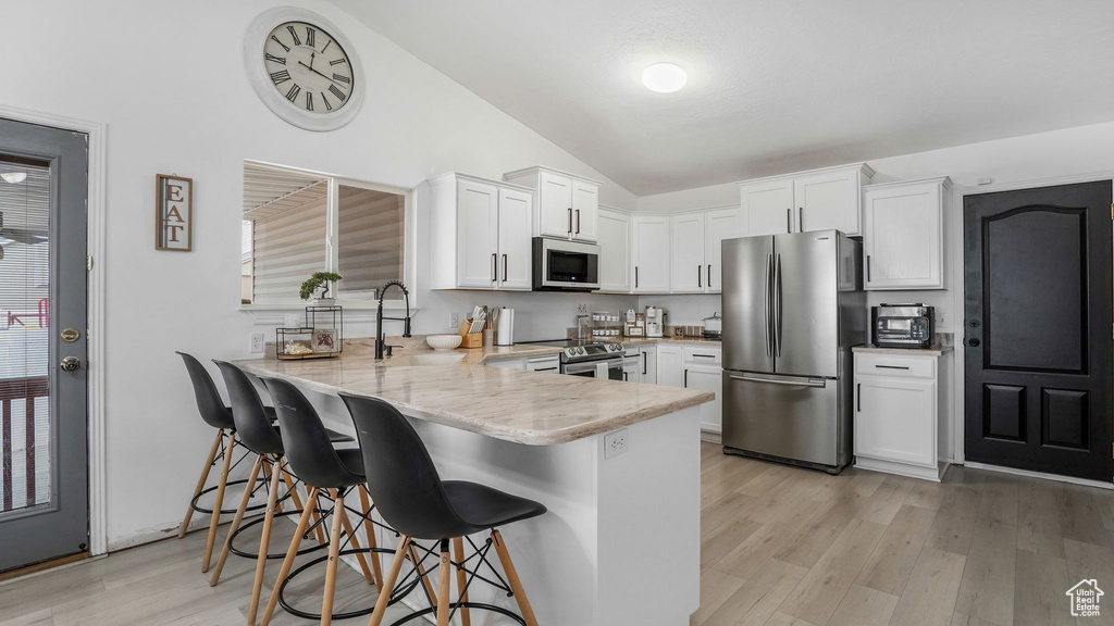 Kitchen featuring a peninsula, light wood-style flooring, a sink, appliances with stainless steel finishes, and vaulted ceiling