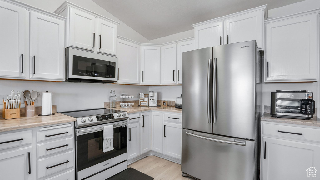 Kitchen with light wood-style flooring, a toaster, stainless steel appliances, white cabinetry, and lofted ceiling