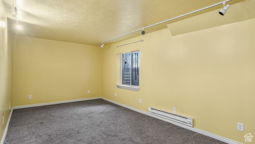 Empty room featuring a baseboard radiator, a textured ceiling, baseboards, dark colored carpet, and track lighting