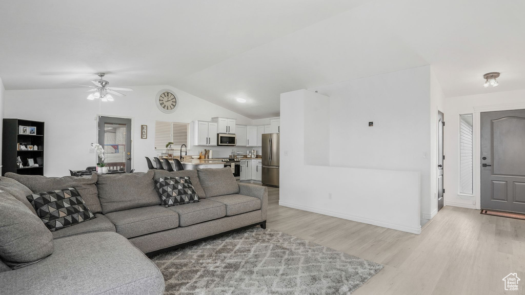 Living area with vaulted ceiling, ceiling fan, baseboards, and light wood-type flooring