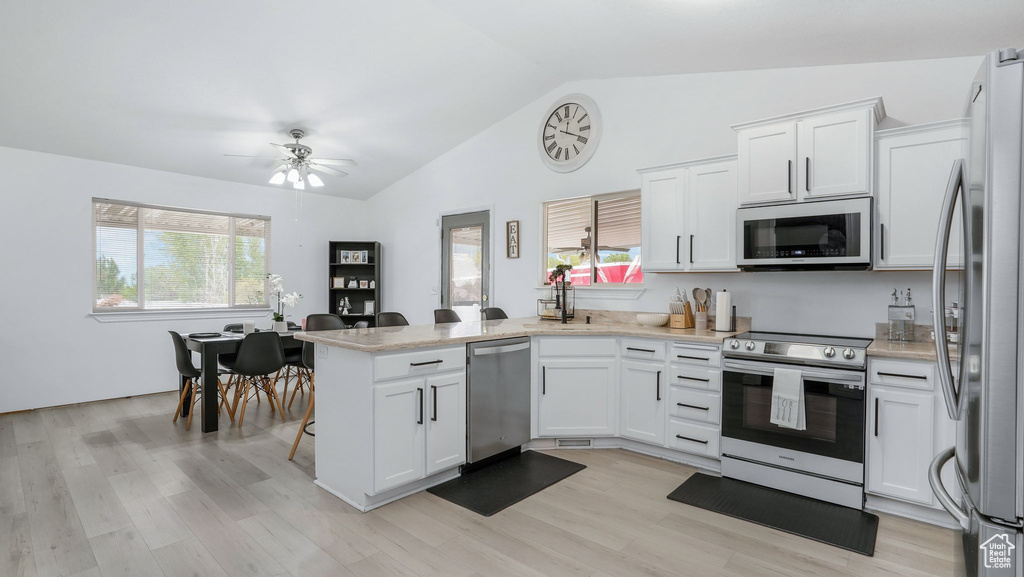 Kitchen with lofted ceiling, plenty of natural light, white cabinetry, a peninsula, and stainless steel appliances