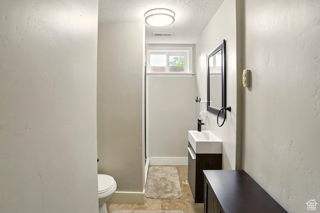 Bathroom featuring toilet, vanity, a textured ceiling, visible vents, and baseboards