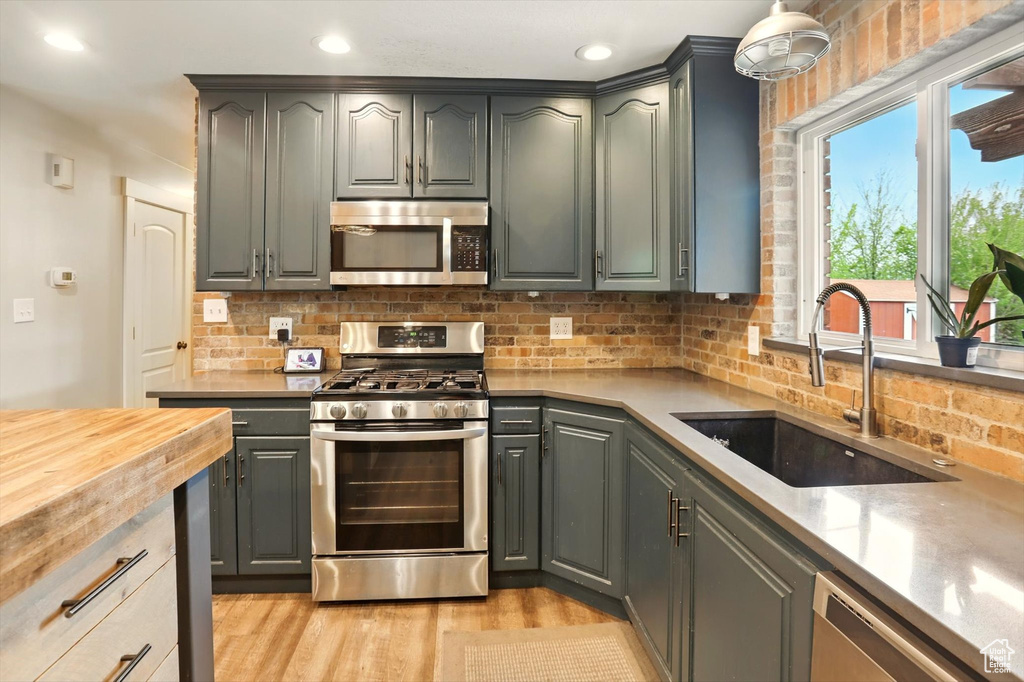 Kitchen featuring light wood finished floors, a sink, wood counters, stainless steel appliances, and tasteful backsplash