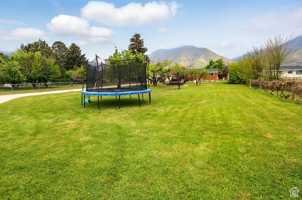 View of yard featuring a mountain view, a trampoline, and fence
